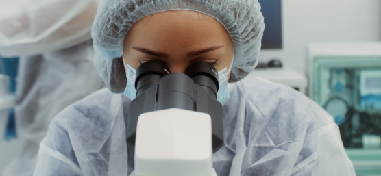 Una persona con traje de protección mira a través de un microscopio