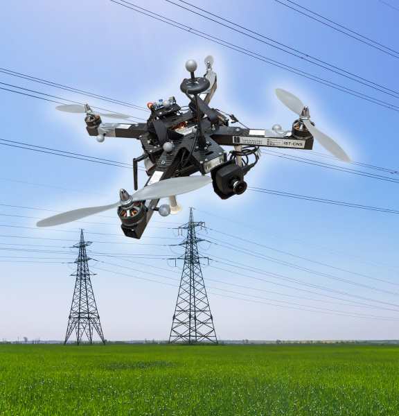 Un dron con cámara IDS sobrevuela delante de líneas de alta tensión y tres postes eléctricos.