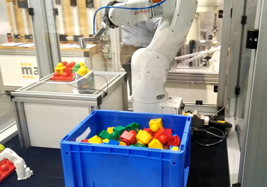 Célula robot mete la mano en la caja con objetos de colores