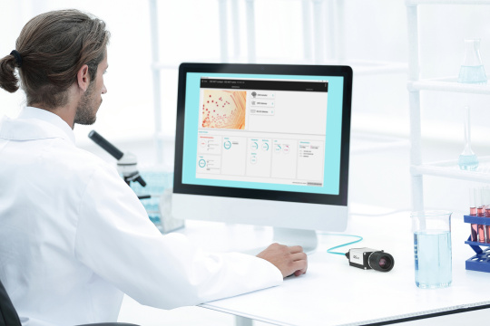 Un hombre está sentado en un laboratorio delante de un PC con el software IDS lighthouse, con una cámara IDS NXT a su lado.