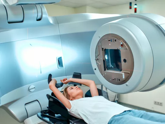 Una mujer tumbada en una camilla frente a una máquina de radioterapia.
