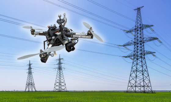 Un dron con cámara IDS sobrevuela delante de líneas de alta tensión y tres postes eléctricos.