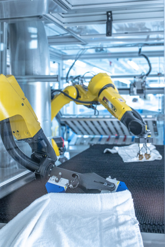 Dos robots despliegan la ropa en una lavandería industrial con ayuda de cámaras IDS 2D y 3D.