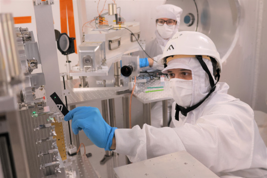 Empleados con ropa protectora alineando los dispositivos de medición en la cámara de vacío.