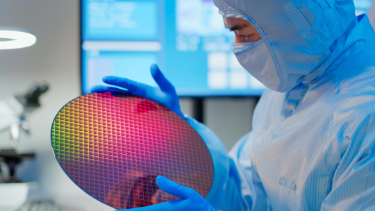 Un hombre con traje azul observa una placa semiconductora redonda en un laboratorio.