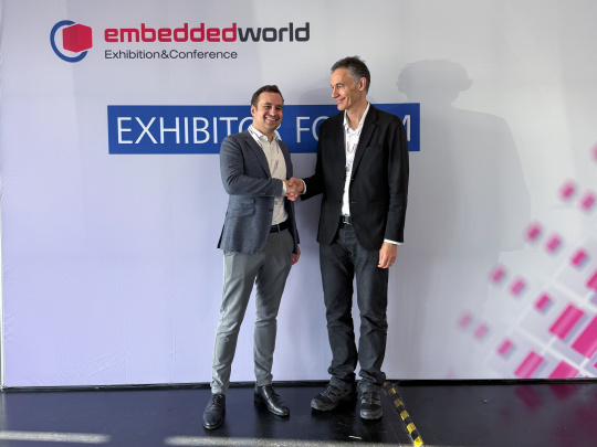 Dos directores generales se dan la mano delante de un stand de la feria Embedded World.
