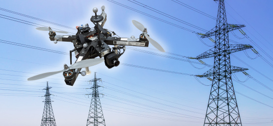 Un dron con cámara IDS sobrevuela delante de líneas de alta tensión y tres postes eléctricos.