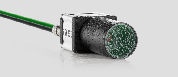 Cámara industrial IDS uEye FA con objetivo, cable y gotas de agua.