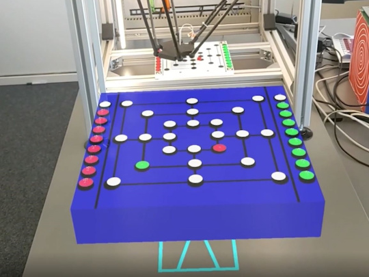 El robot juega al molino en la caja, delante de la caja el tablero de juego equivalente para jugar contra el robot