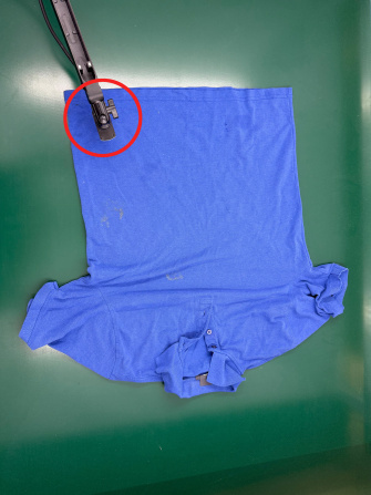 Camiseta azul sobre fondo verde, cámara uEye XC en brazo móvil inspeccionando desde arriba.