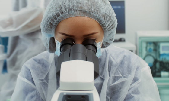Una persona con traje de protección mira a través de un microscopio