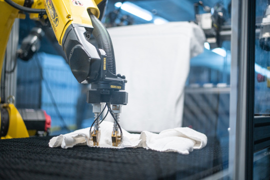 Un robot amarillo despliega una toalla en una lavandería industrial.